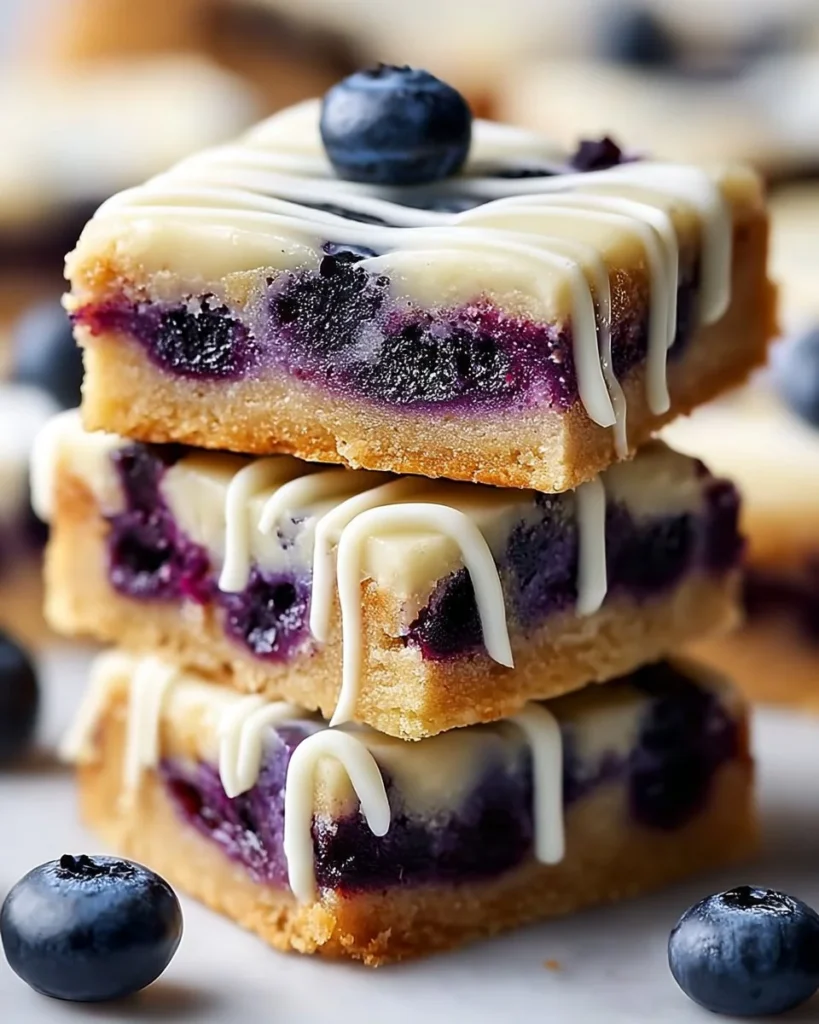 Blueberry lemon cookie bars topped with white chocolate drizzle on a plate.