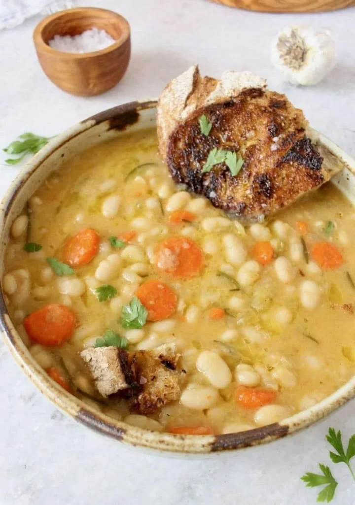 A bowl of Mediterranean Italian White Bean Soup garnished with herbs and spices.