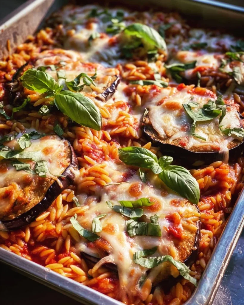 One Pan Eggplant Parmesan Orzo dish served in a skillet, topped with cheese and herbs.