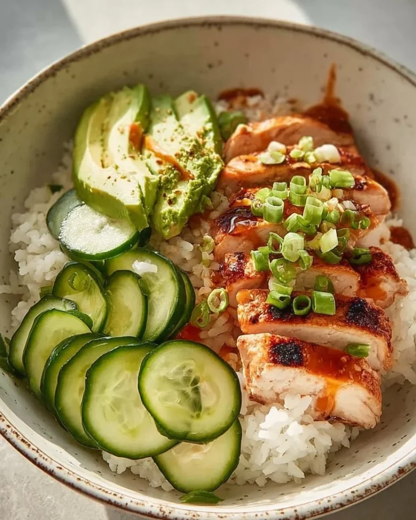 Spicy chicken rice bowl with fresh cucumber, avocado, and flavorful seasonings.