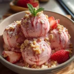 Bowl of strawberry ice cream topped with fresh strawberries and mint leaves.
