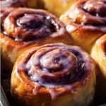Delicious homemade ube cinnamon rolls topped with purple icing and cinnamon.